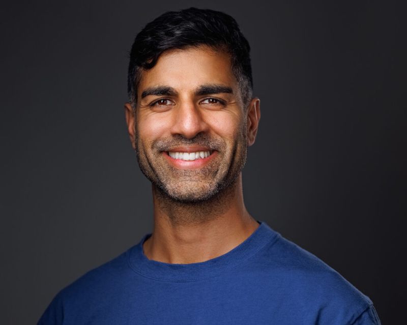 Khurram Naik smiling in a blue shirt against a dark grey background